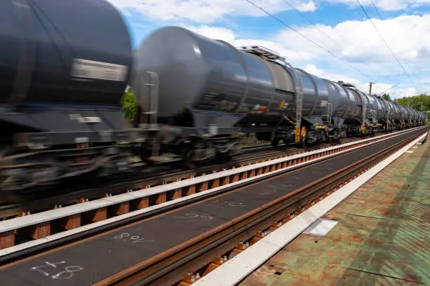 Blurry photo of railroad tank cars in motion, on a metal bridge over the river.