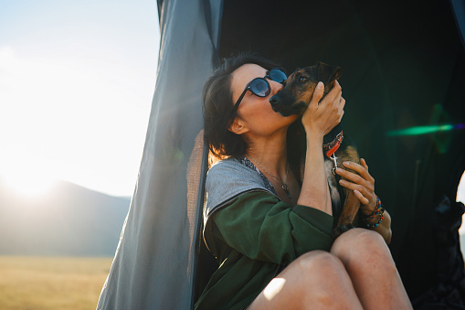 Young woman with her pet dog in a car rooftop tent, waking up in the morning.