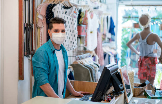 empresário que trabalha em uma loja de roupas usando uma máscara facial - clothing store sales clerk usa clothing - fotografias e filmes do acervo