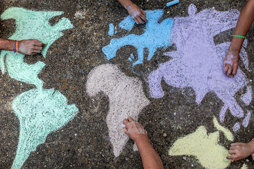 A group of people drawing with colored chalks on the floor with his hands in the street a map of the world