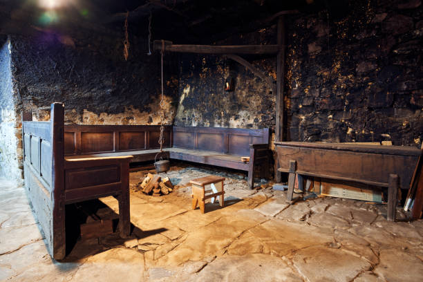 cozinha antiga de mais de 300 anos com sua panela pendurada em um arco de madeira e correntes para fazer o fogo com um banco ao seu redor, um banquinho e uma cesta de pão onde o pão foi fermentado - old old fashioned black 100th anniversary - fotografias e filmes do acervo