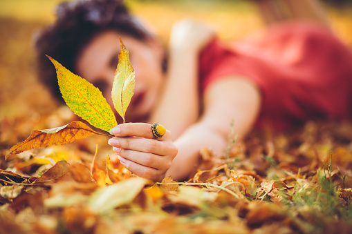 Young beautiful caucasian woman lying on autumn leaves.