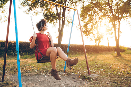 Young beautiful caucasian  woman on a swing in a park on beautiful sunny autumn day.
