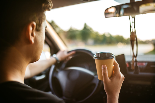 Young man drinking coffee while driving a car.