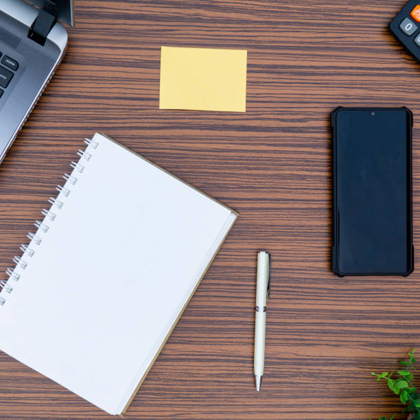 istock An office table working enviroment. Notepad, sticky note, pen plant, calculator and a lap top on a brown striped zebrawood design table top. Must have objects while working from home during Covid-19 1271780300