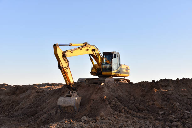 istock Yellow excavator during earthmoving at open pit on blue sky background. Construction machinery and earth-moving heavy equipment for excavation, loading, lifting and hauling of cargo on job sites 1271783727