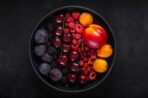 raspberries, currants, apricots, peaches, cherries and plums in a black plate