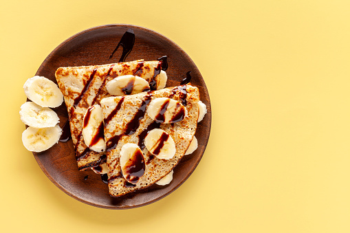 Crepes on a wooden plate on a yellow background. Copy space