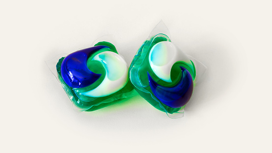 pair of blue and green wash capsules with detergent gel for laundry automatic machine isolated on white background