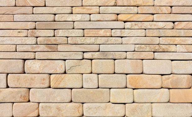 The wall is lined with hewn rounded yellow sandstone stone. Wall background and texture of hewn rounded yellow sandstone stone, close-up. roughhewn stock pictures, royalty-free photos & images