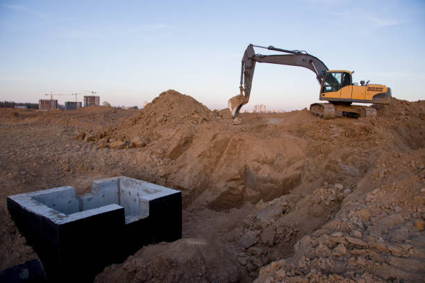 Excavator working at construction site on earthworks. Backhoe digs ground in pit for laying concrete sewer wells and sewage pipes. Installing underground storm systems of water main and sanitary sewer excavadora trabajando en obra en obras de tierra. la retroexcavadora excava el suelo en el pozo para la colocación de pozos de alcantarillado de hormigón y tuberías de alcantarillado. instalación de sistemas de tormentas subterráneas de alcantarillado