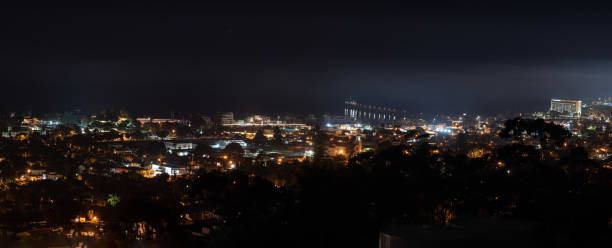 Panoramic view of the coastal city of Ventura nestled against the Pacific Ocean at night with town lamps shining bright with a fog haze hovering overhead.