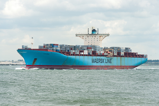 Ships float across the North Sea. Windmills in the background. Sea port in the Netherlands. A lot of cranes for loading goods. Different ships and barges.