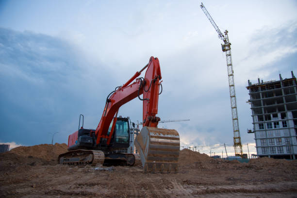 istock Excavator working at construction site on earthworks on evening sunset. Backhoe digs ground for roadwork. Tower cranes in action construction of a new multi-storey buildings in night 1271793847