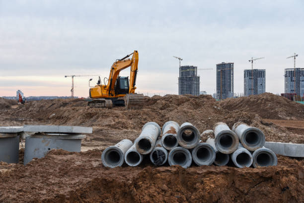 istock Excavator in action at construction on earthwork. Laying concrete drainage pipes of underground storm heating sewer system. Installation of water main, sanitary sewer and concrete sewer wells 1271795894