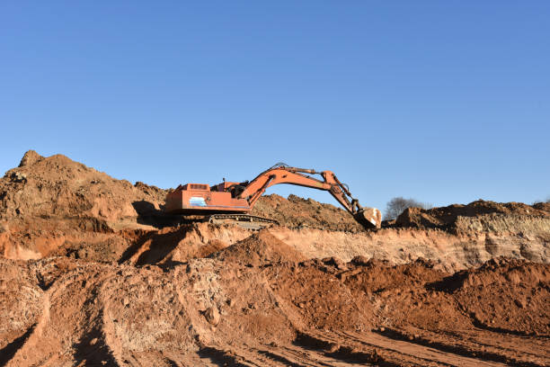 istock Yellow excavator during earthmoving at open pit on blue sky background. Construction machinery and earth-moving heavy equipment for excavation, loading, lifting and hauling of cargo on job sites 1271796007