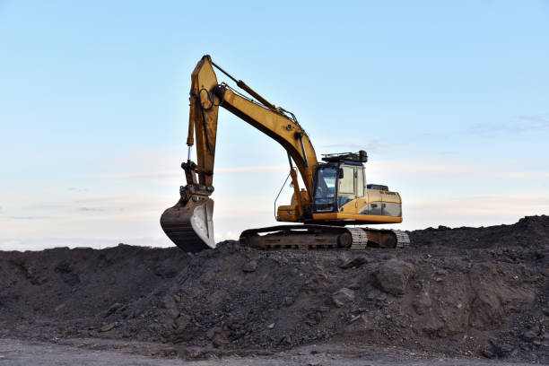 istock Excavator working on earthmoving at open pit mining on sunset background. Backhoe digs gravel in quarry. Construction machinery for excavation, loading, lifting and hauling of cargo on job sites 1271798132