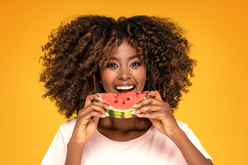 Beautiful young afro girl eating slice of watermelon .