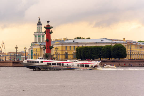 A hydrofoil ship goes along the Neva River in front of the building of the Zoological Museum and the Rostral Column. The background is blurred stock photo