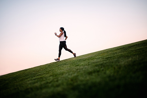 A fit and active African American woman on an evening jog in Washington state, enjoying the beauty of the outdoors and vitality she feels from a healthy lifestyle.