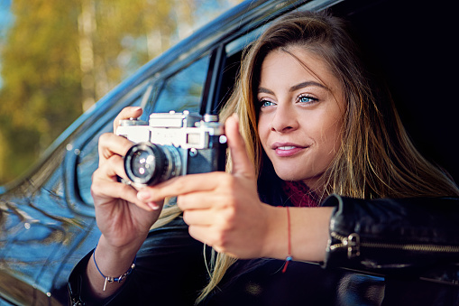 Beautiful woman is taking pictures using vintage camera from a moving car