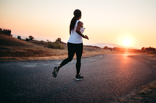 A rear view of a fit and active African American woman on an evening jog in Washington state, enjoying the beauty of the outdoors and vitality she feels from a healthy lifestyle.