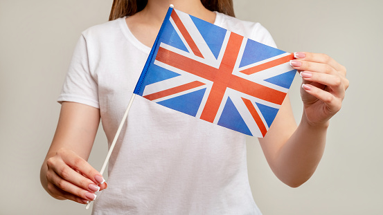Union Jack. United Kingdom. Woman holding British flag with red cross on white blue isolated on blur neutral background. Official national symbol of UK. Great Britain.