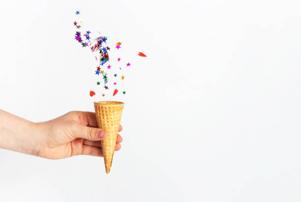 istock A woman's hand holds waffle cone and falling confetti on white background 1271846075
