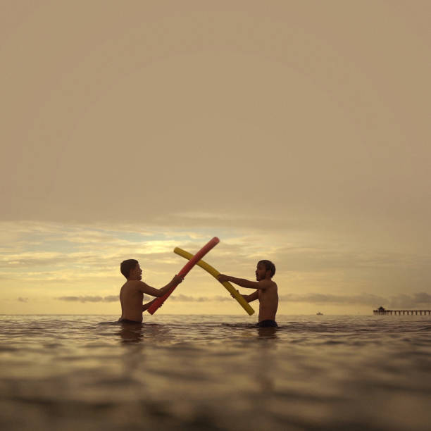 Two young guys noodles fight on the beach
