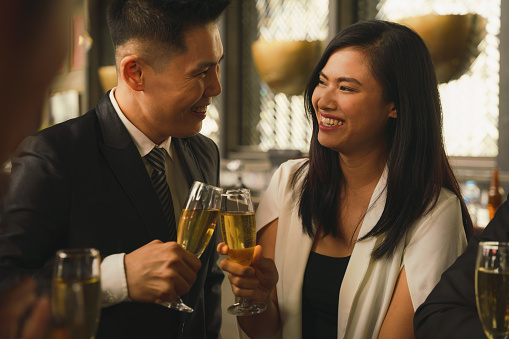 asian business couple toasting and clinking wine or champagne together to celebrate friendship