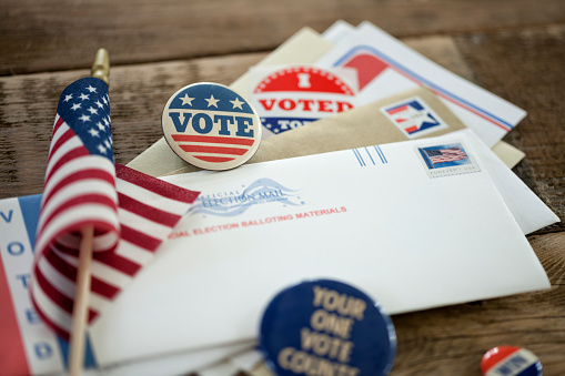 Absentee Ballot and campaign buttons on a wood surface.