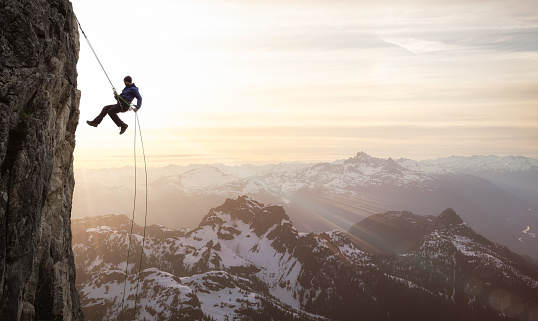 Epic Adventurous Extreme Sport Composite of Rock Climbing Man Rappelling from a Cliff. Mountain Landscape Background from British Columbia, Canada. Concept: Explore, Hike, Adventure, Lifestyle