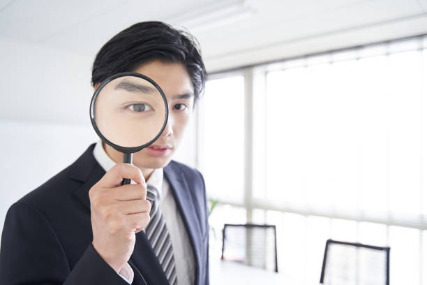 a japanese male businessman looking through a magnifying glass in a conference room - business person suspicion clothing well dressed imagens e fotografias de stock