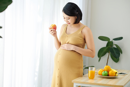 Pregnant beautiful girl holds apple, takes good care of herself by eating healthy foods.