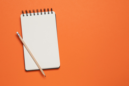 Spiral notebook and pencil on orange background