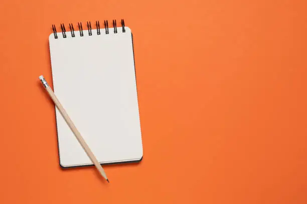 Spiral notebook and pencil on orange background