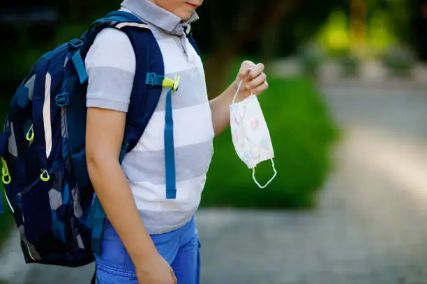 Close-up of kid boy with medical mask and backpack or satchel. Schoolkid on way to school. child outdoors. Back to school after quarantine time from corona pandemic disease lockdown. no face