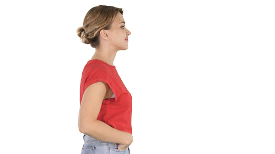 Medium shot. Side view. Young beautiful girl with hands in pockets walking on white background. Professional shot in 4K resolution. 006. You can use it e.g. in your commercial video, business, presentation, broadcast