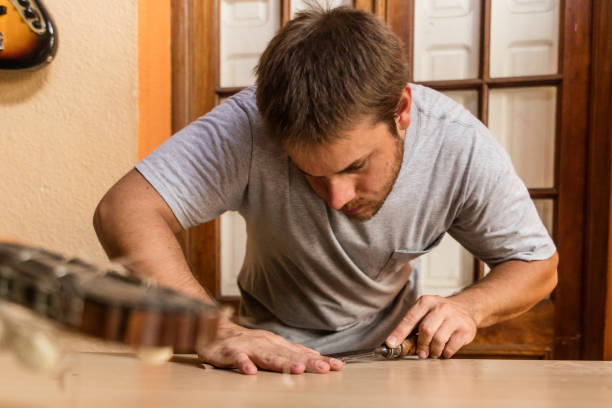 istock Young instrument maker is chinceling a guitar part at studio workbench 1271870427