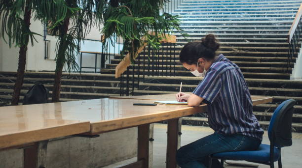 Left angle isolated young college student taking notes alone in the library stock photo