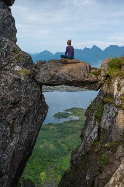 asiatische frau sitzt auf djevelporten oder teufelstor in floya bergwanderweg in der sommersaison. svolvaer fischerdorf auf der insel lofoten, skandinavien - austvagoy stock-fotos und bilder