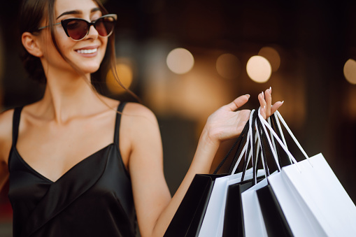 Fashion woman enjoying shopping. Elegant woman wears black dress holding black and white shopping bags. Black friday, sale, consumerism, lifestyle concept.