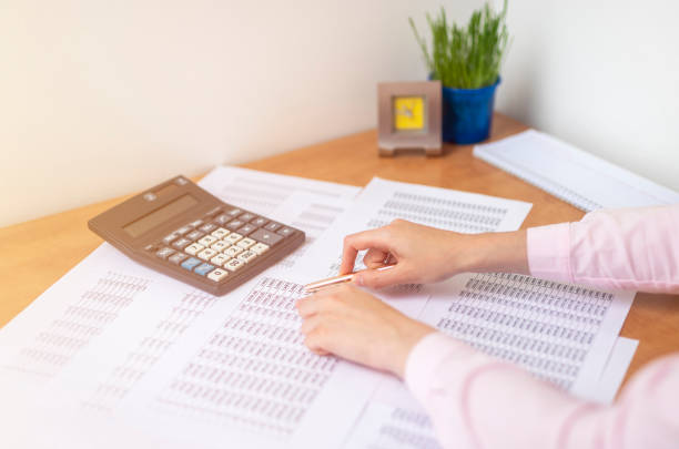 istock female accountant or banker making calculations sitting at office table with documents with tables on desk pointing at digits on documents. Savings, finances and economy concept 1271877258