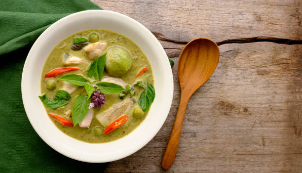 istock Famous internationally renowned Thai green coconut curry 'Gaeng Keow Wan Gai', with chicken, in a white bowl on a green cloth and with a serving spoon next to the bowl, sitting on an old worn wood table background. 1271879366