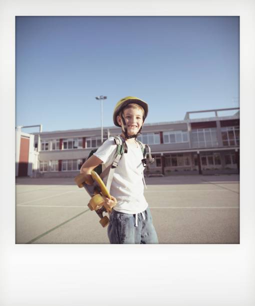 Instant photo of a schoolboy Instant photo of a cheerful schoolboy carrying his skateboard and spending time in his schoolyard; returning to school after summer vacation. skating photos stock pictures, royalty-free photos & images