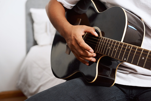 Shot of a young man playing the guitar while sitting at home