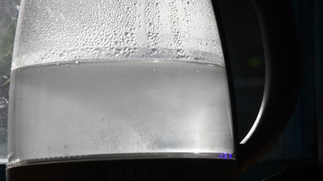 Close-up of uncleared boiling water in old transparent kettle with limescale