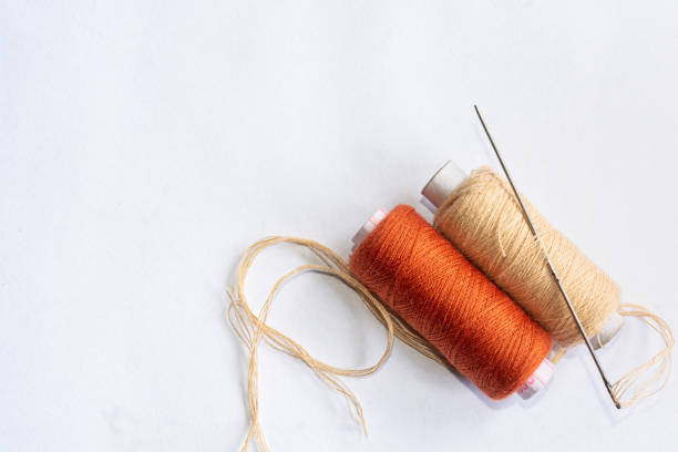 Brown and cream color sewing thread spools with needle on isolated white background. Top view and copy space.