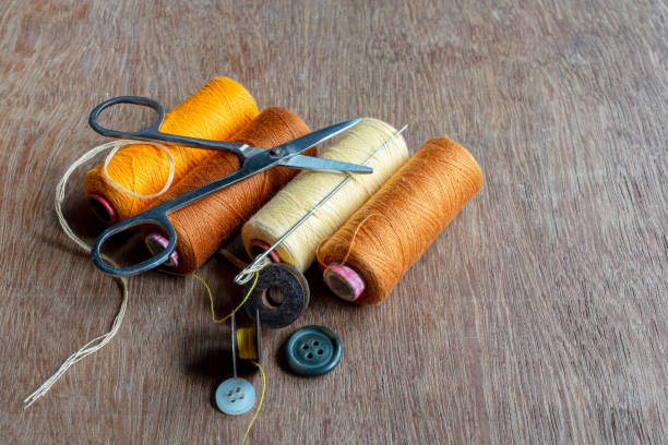 istock Four different shades of yellow and brown colored sewing thread spools with needle and sewing accessories on brown wooden background. 1271888133