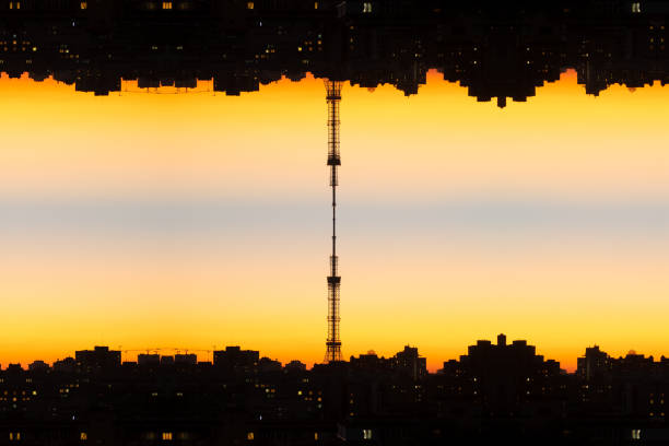 Upside down orange cityscape at sunset, reflected vertically, with a tower connecting the two cityscapes in the center. Reflected cityscape that looks like a phonogram of audio track.